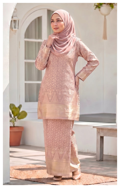 woman wearing Kurung Moden Baby Pink brocade front view round neck design in an outdoor setting.